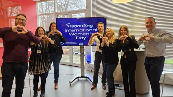 Seven team members posing for group photo on International Women's Day holding up heart shaped hands