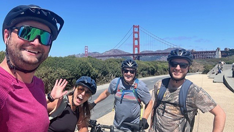 Four LSB team members in bike helmets posing near Golden Gate Bridge