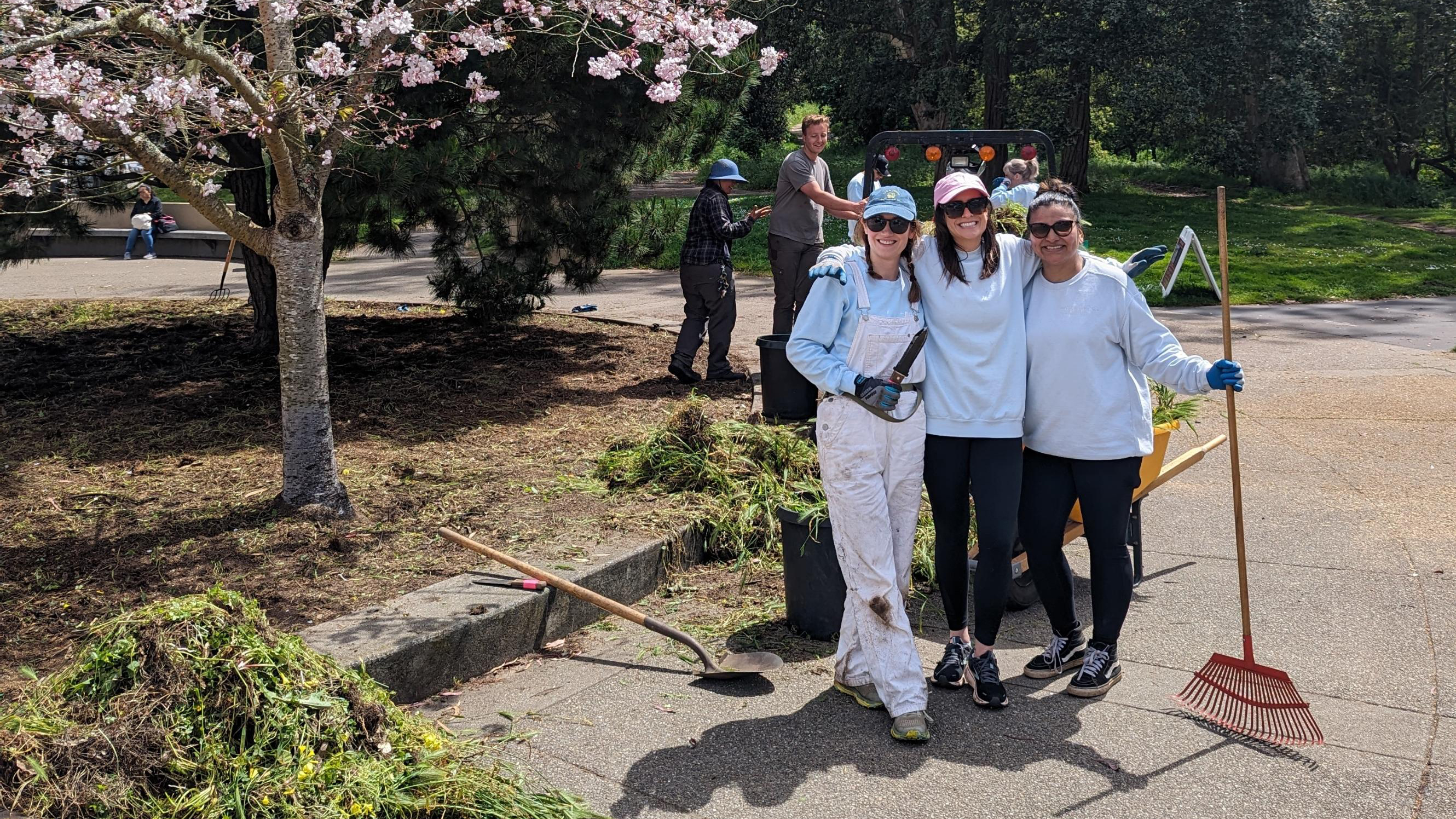 Three LSB team members holding a rake at outdoor park cleanup volunteering event