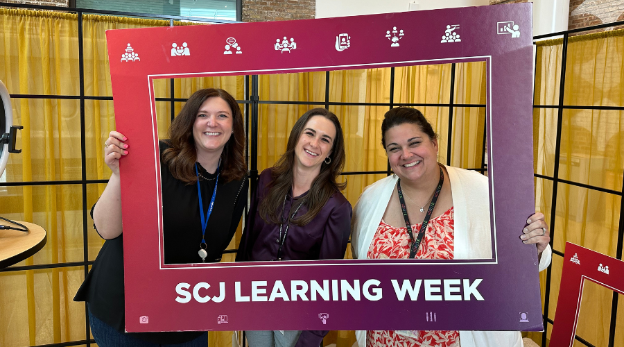 three SCJ team members pose for a photo with a SCJ Learning Week photo frame prop