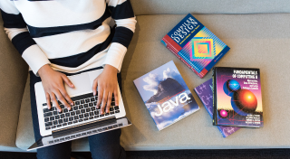 Person typing on laptop with three books sitting next to them on computer coding