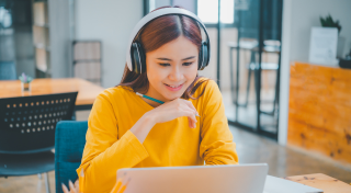 Woman with headphones on looking at computer screen watching a video