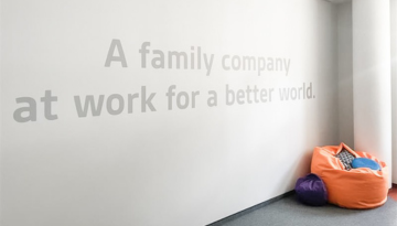 Photo of a wall featuring the SCJ tagline, ‘A Family Company at Work for a Better World,’ with a chair positioned in the corner