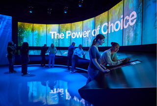 People at exhibit with digital screen with "the power of choice" with blue ocean imagery