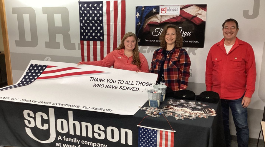 Three team members standing at table with flag thanking Veterans for service