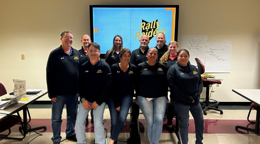 Team of Rally Raider volunteers posing together in a group photo with team logo in background