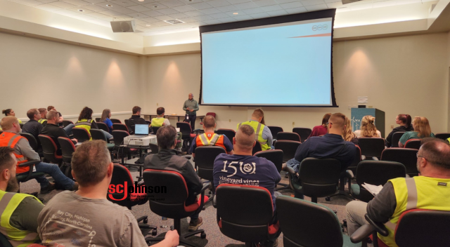 Presenter standing near podium with presentation on screen behind him