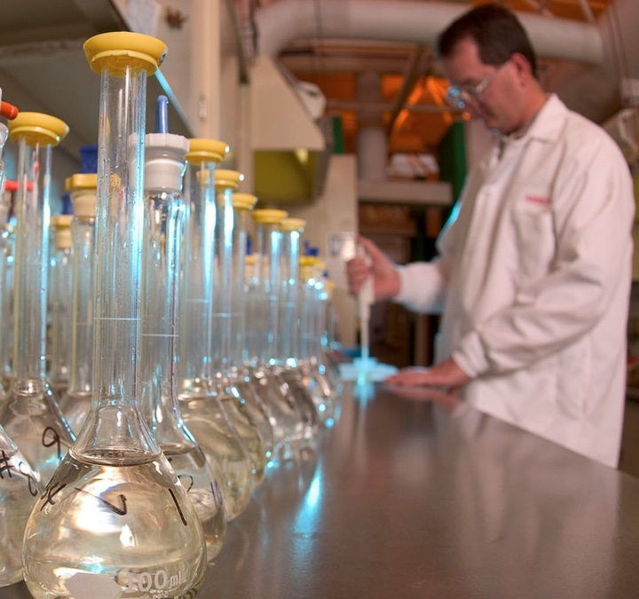 Man wearing white labcoat next to chemical flasks