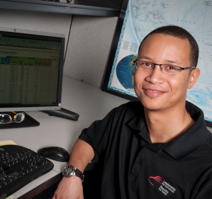 Man smiling at his desk next to a computer and keyboard