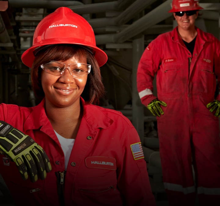 Man and woman wearing red coveralls, hard hats, and protective glasses