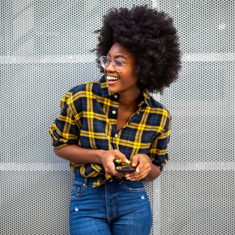 Happy smiling young black woman with afro hair holding cellphone