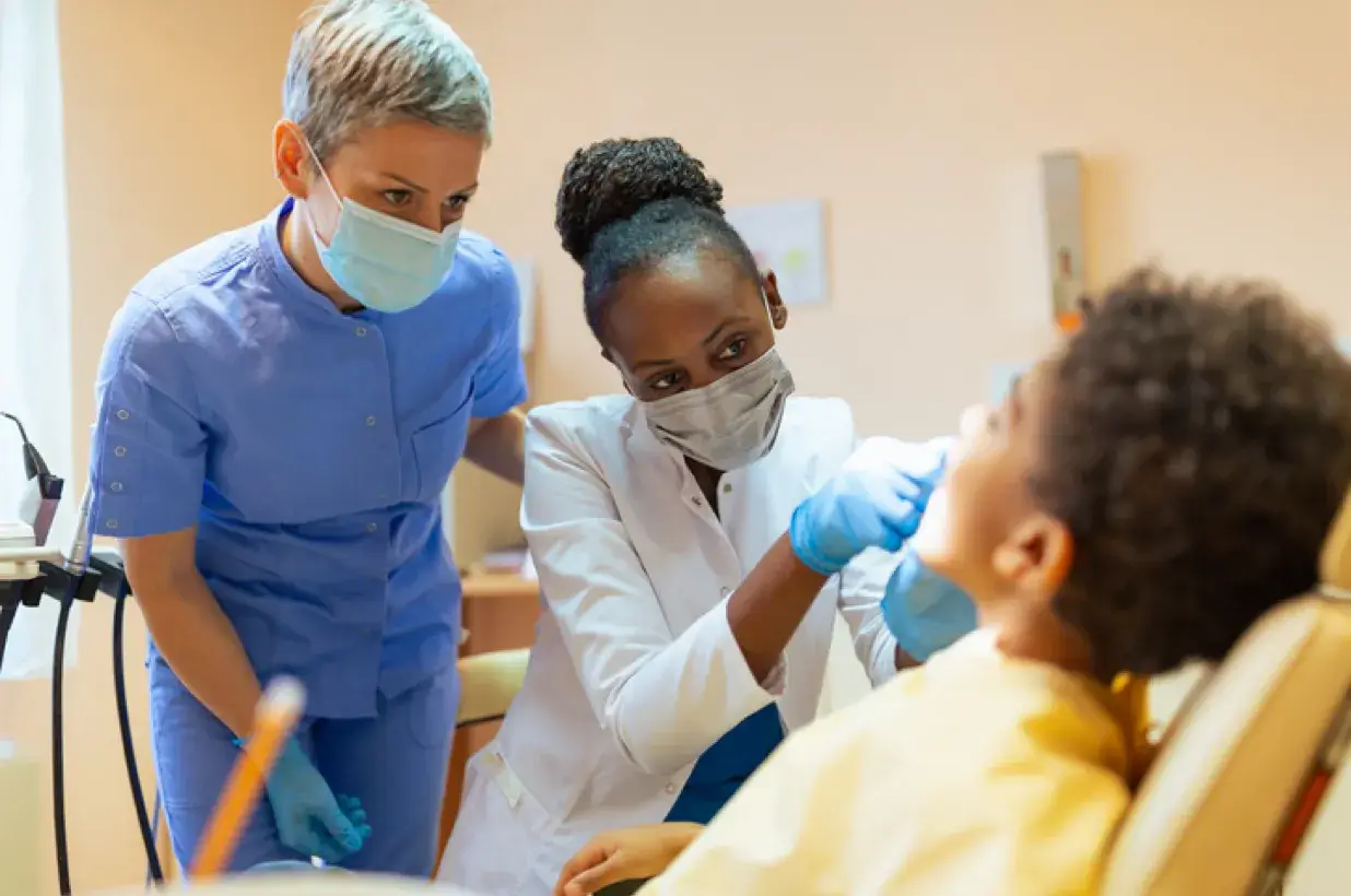 female dental assistant looking over the shoulder of another dental assistant as she performs a dental procedure on a patient