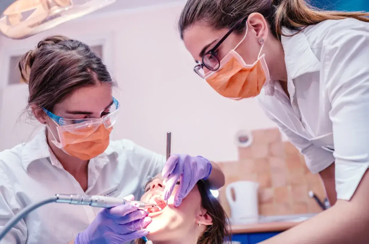 female dental assistant watching as another performs a dental procedure on a patient