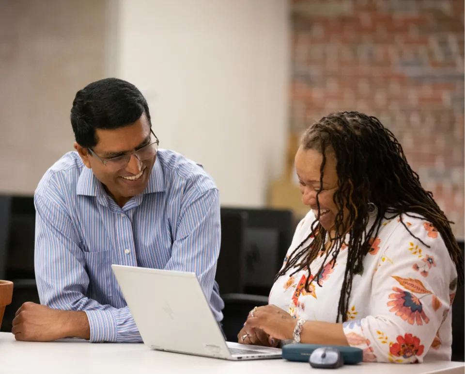 Two people smiling while working on a computer