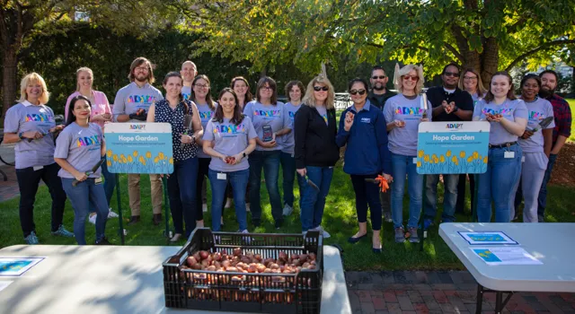 large group smiling and holding a Hope Garden sign