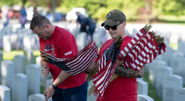 two men placing flags at a cemetary