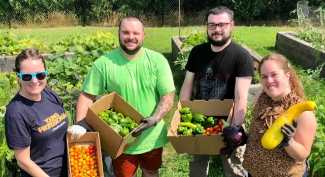 people smiling for the camera while standing in a garden holding vegetables