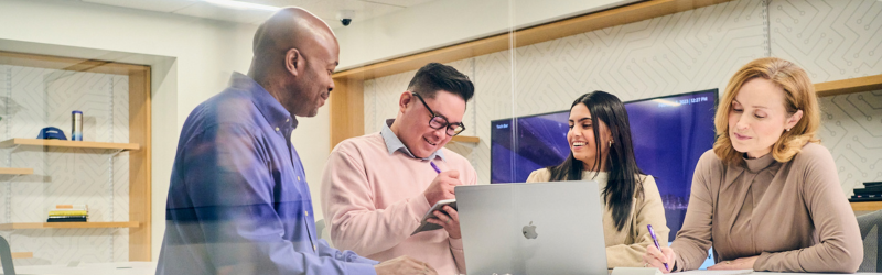 two women and two men working in an office and looking at a computer, smiling