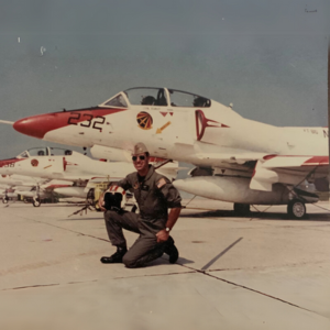 Man in a flight suit in front of a military aircraft.