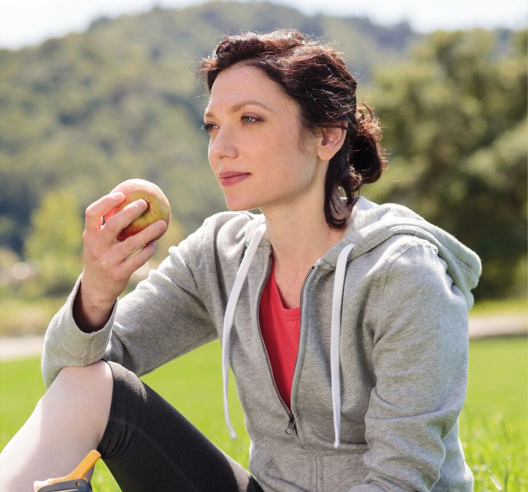 Woman in park wearing yoga clothes and eating an apple