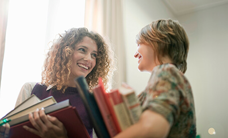 Women holding books and smiling at each other