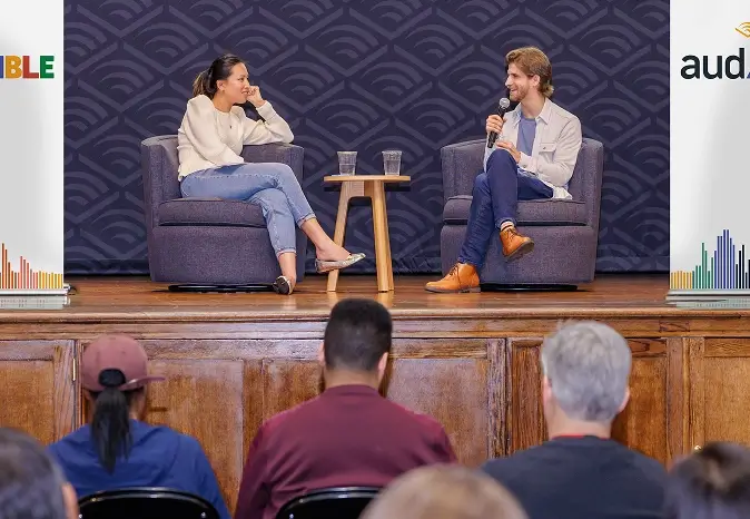 Two people sitting on a stage talking to a group of people