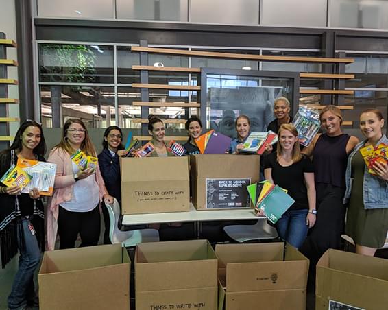 Group of employees displaying school supplies that are about to be packed in boxes