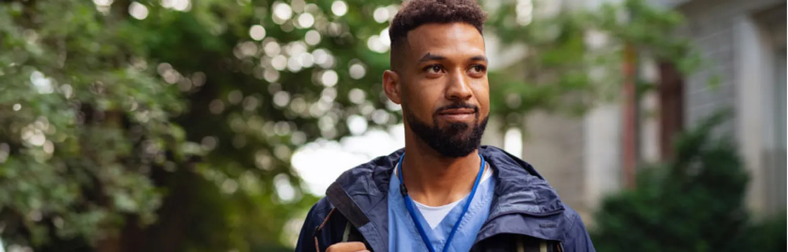 Man wearing surgical scrubs smiling, while standing outside