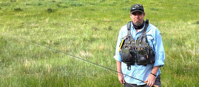 Sean holding a fishing rod standing in a marsh.