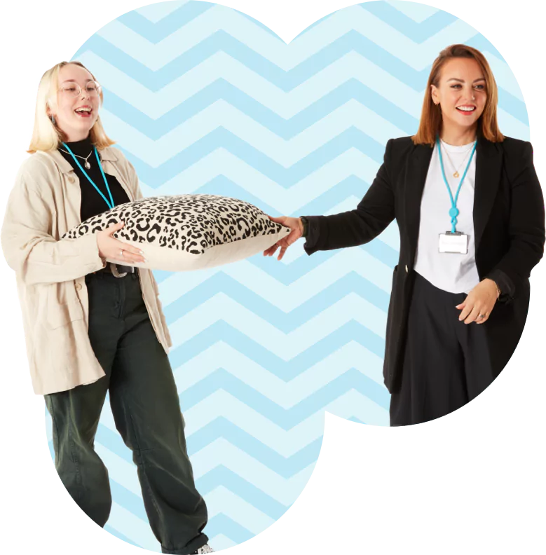 Two women happily posing and holding a pillow.