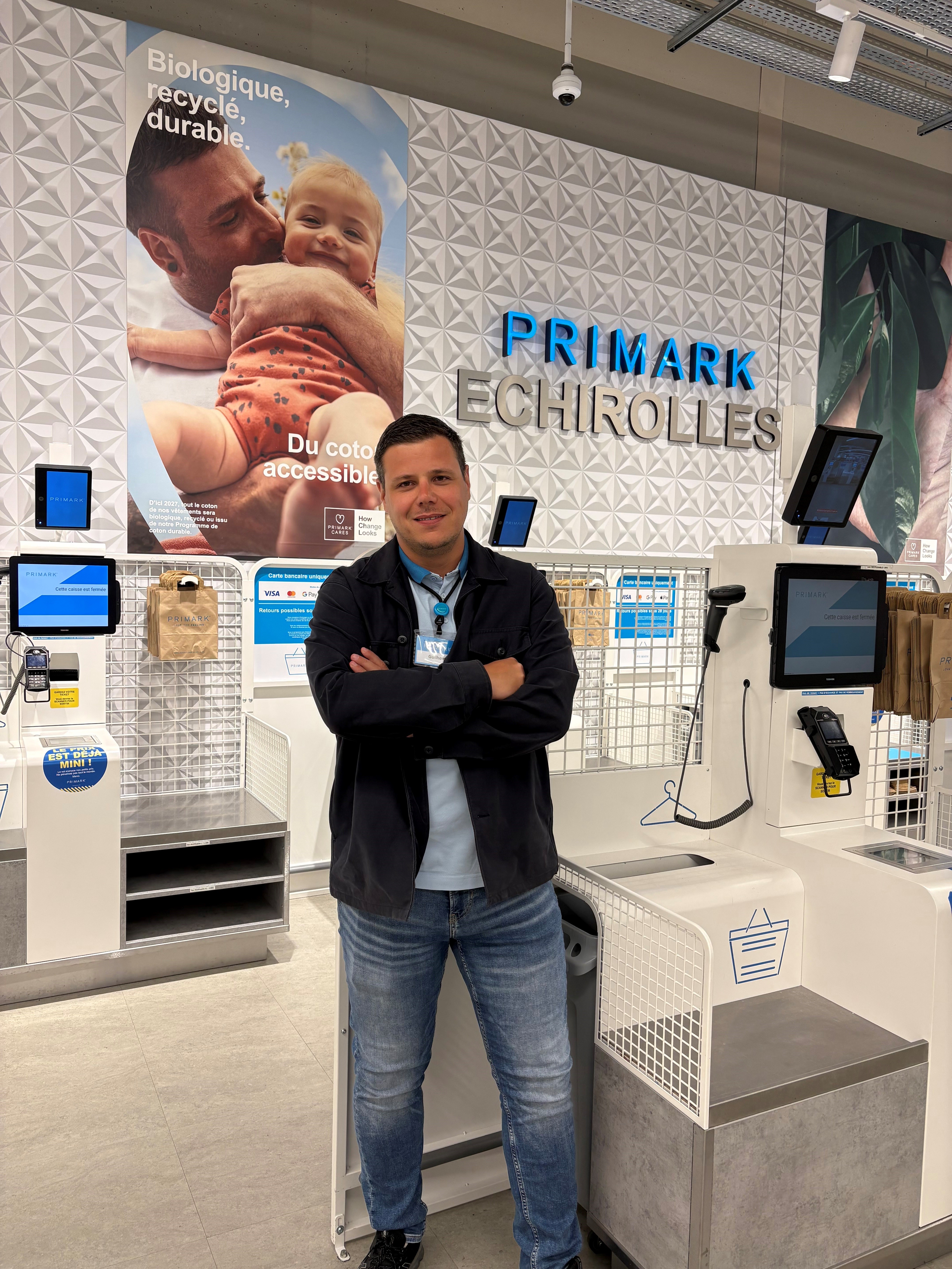 Colleague standing at self checkouts with arms folded