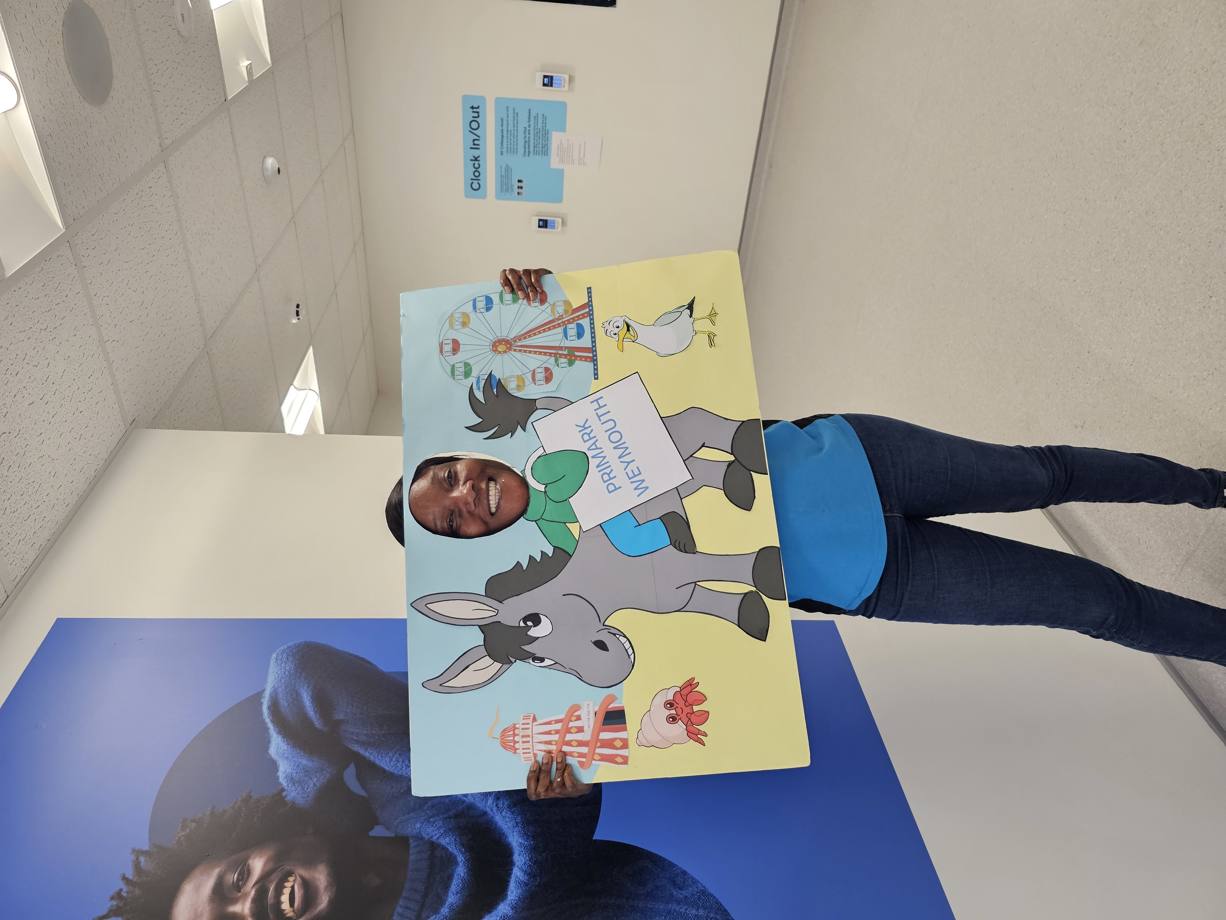 Colleague smiling ins tore with her face through a poster of a donkey