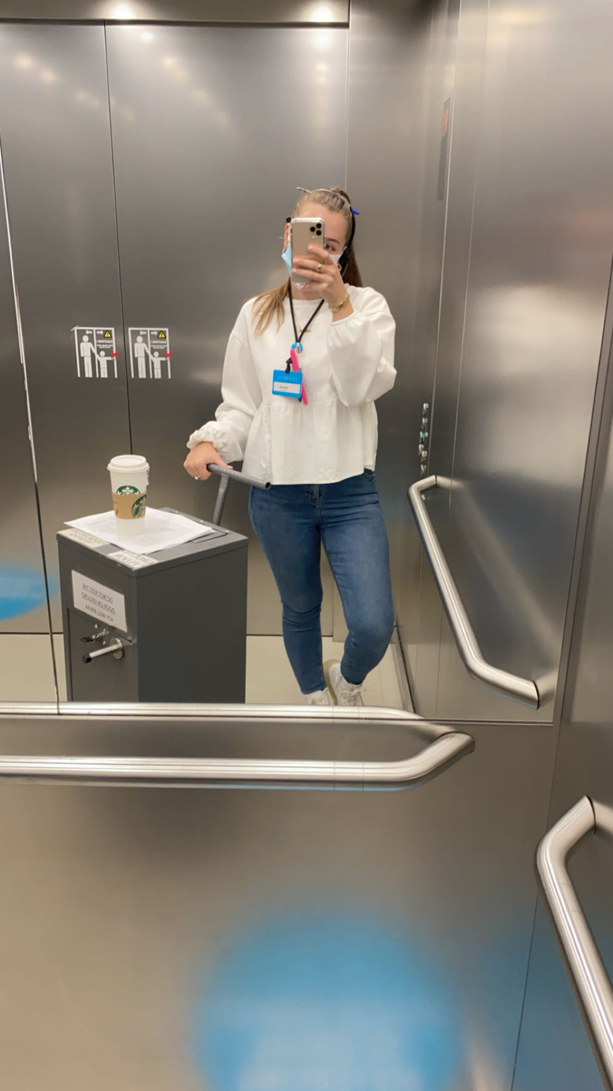 Female colleague taking a picture in a lift mirror while pushing a trolley