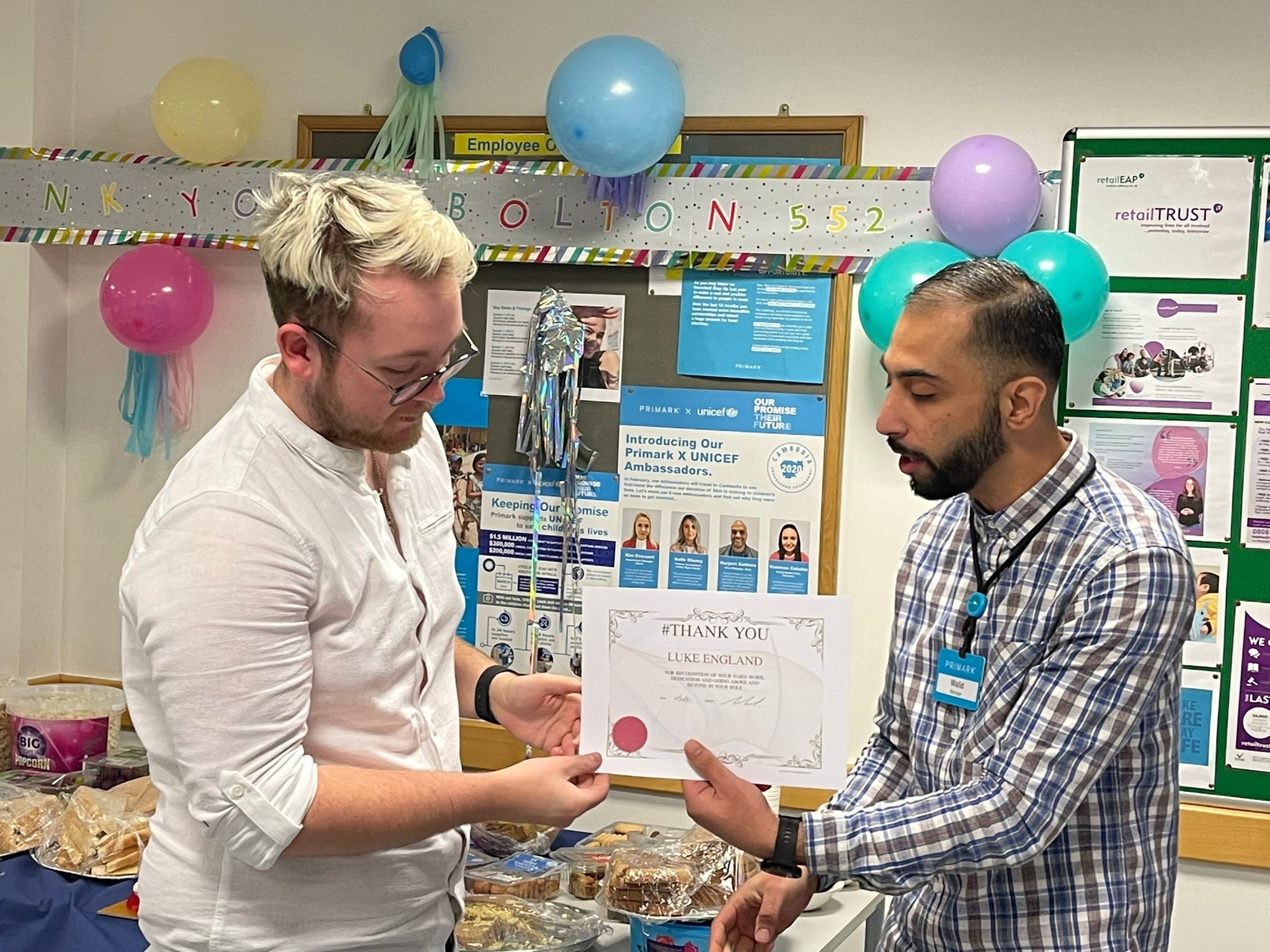 Male colleague giving an award certificate to another male colleague in a Primark strore office