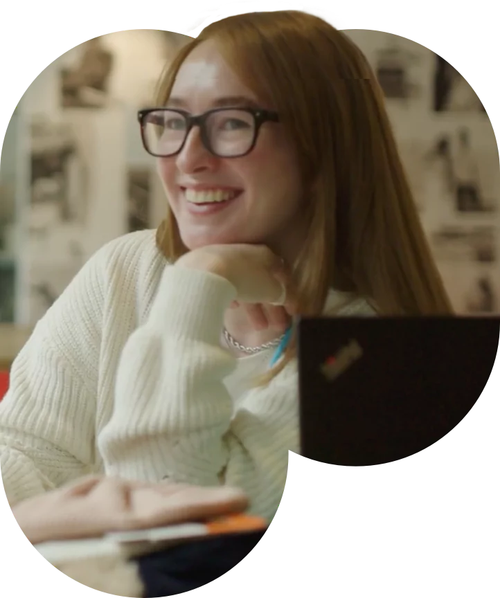 Female with glasses next to laptop smiling