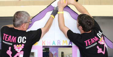 Two men wearing Team OC t-shirts putting up a wooden facade for a charity project