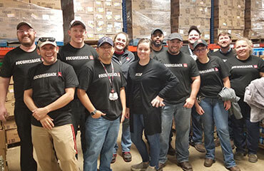 Amarillo employees proudly stand in front of stacked pallets full of many boxes of food