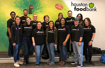 Houston employees pose in front of a wall size poster for Houston Food Bank