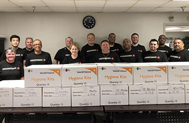 Houston team members stand behind a tall and wide stack of hygiene kit boxes