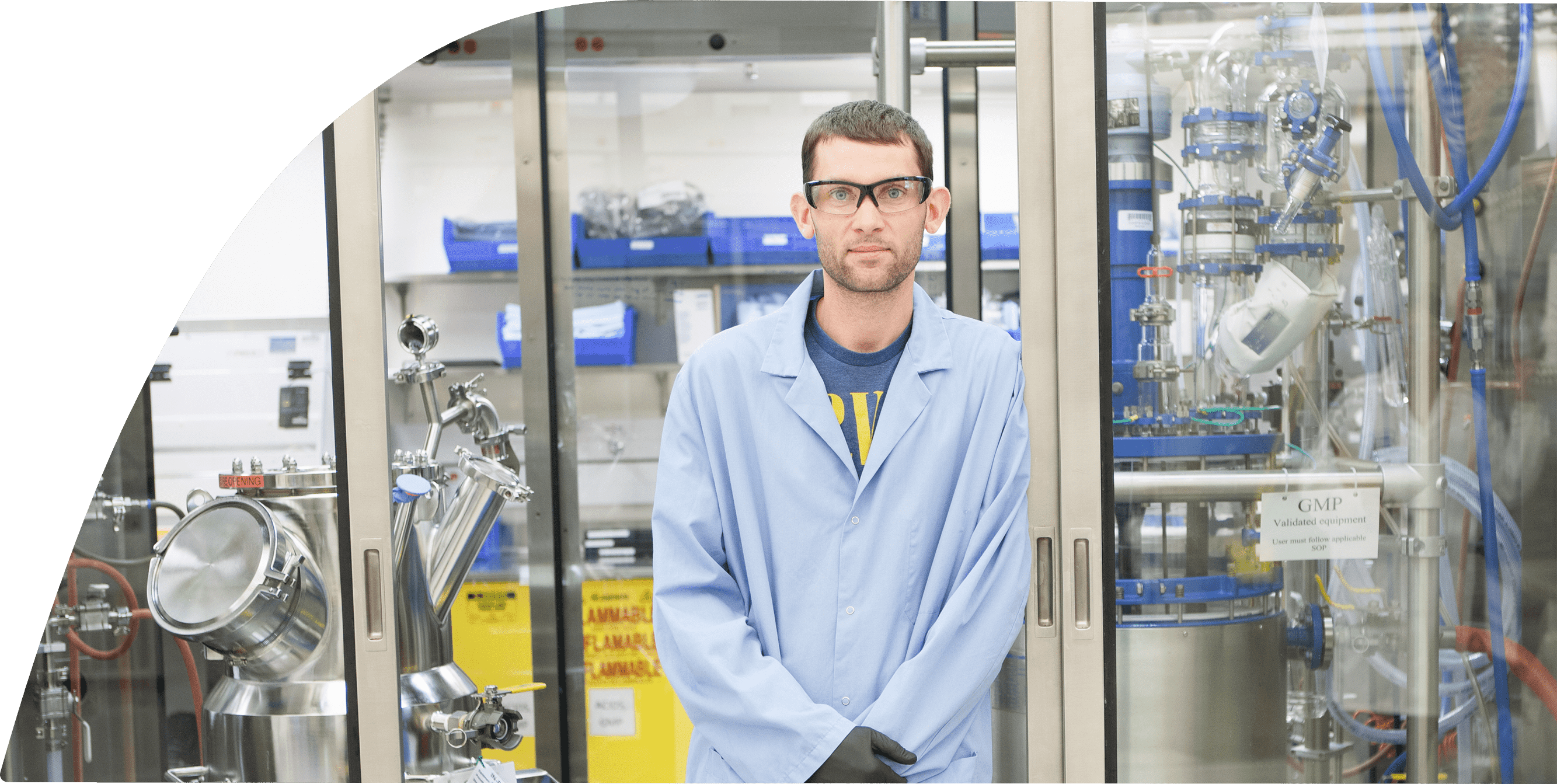 A man in safety goggles and lab coat is standing in a lab setting