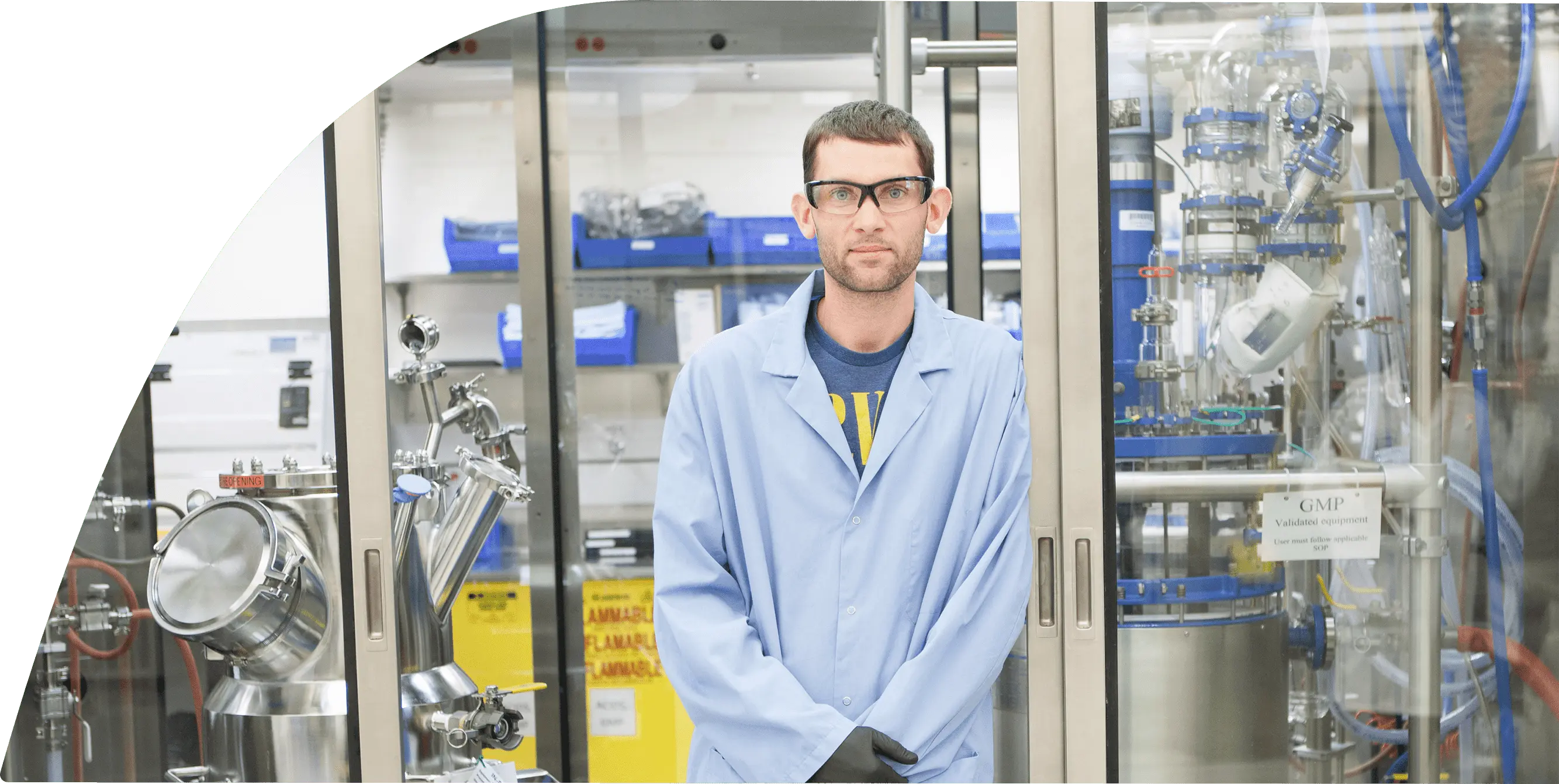 A man in safety goggles and lab coat is standing in a lab setting