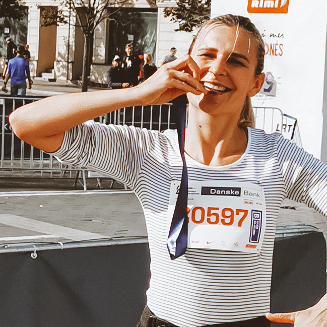 Donata, a female Project Leader from Lithuania, after a run, biting on a running medal, smiling