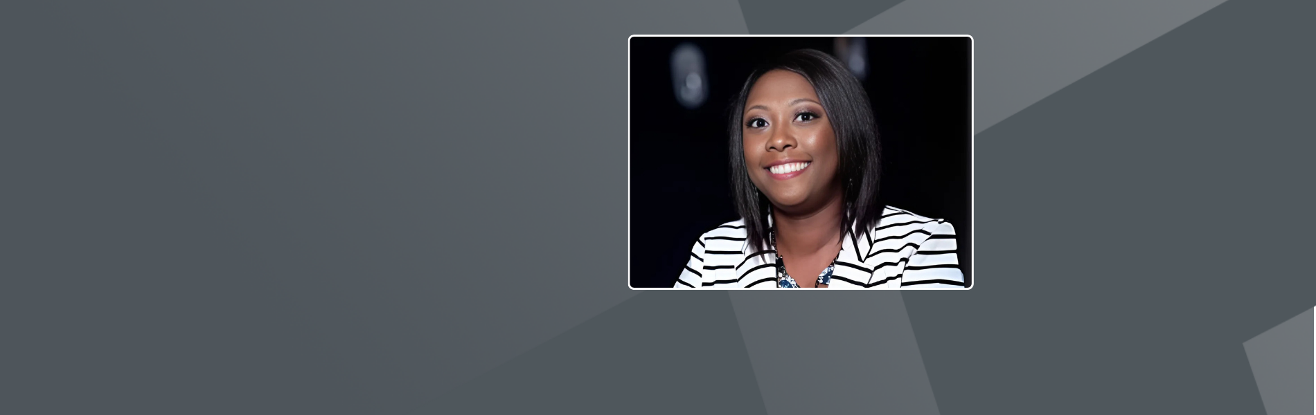 Marlayna, a Black-American woman, smiling at the camera. She is wearing a black and white striped blazer over a blue top, complemented by a statement necklace, against a dark background.