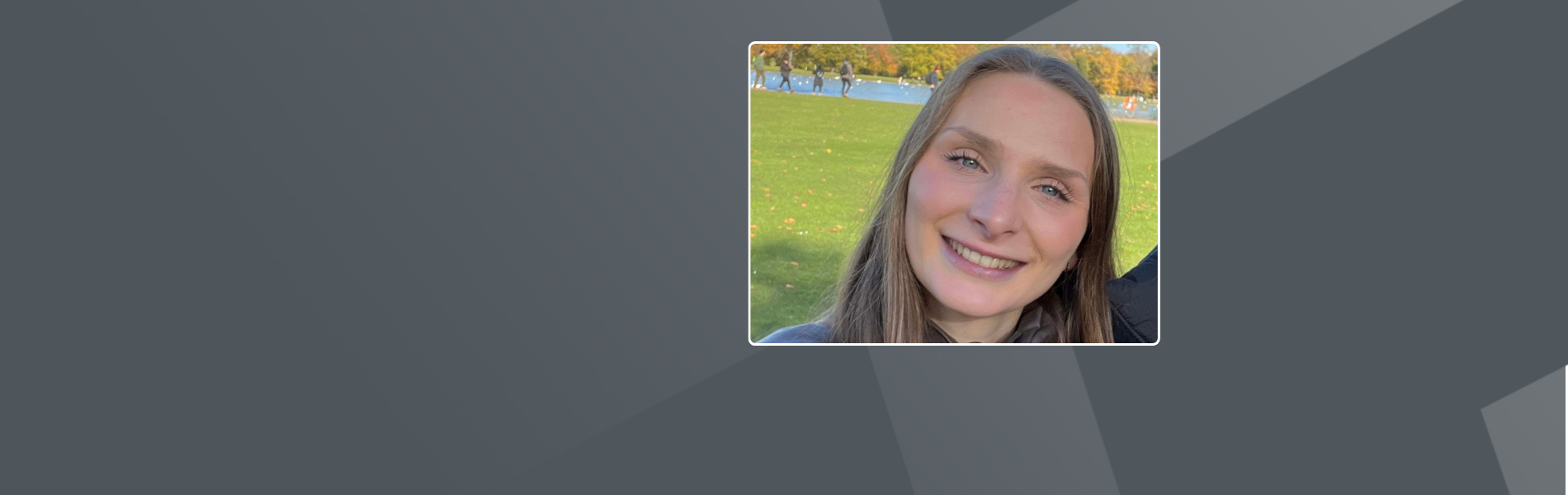 Katherine, long brown hair, smiling at the camera while sitting on a grass field