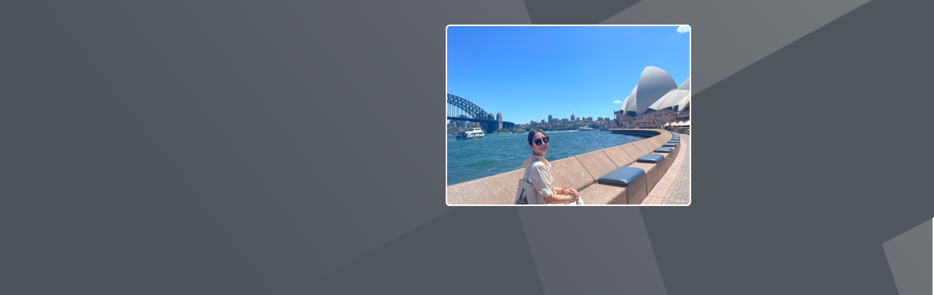 Yena, a Korean Woman in Sydney, Australia. She is sitting on a bench and in the background is the Opera House and Harbour Bridge.  She has dark tide back hair, wears sunglasses and a beige dress.