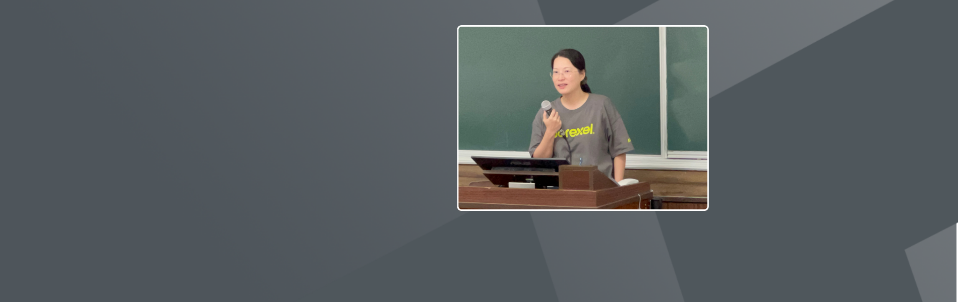 A woman with a black ponytail is holding a microphone before a black board.