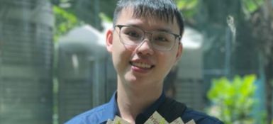 Di Kent, a short-haired man wearing glasses and a blue shirt is smiling while holding a bouquet of flowers.