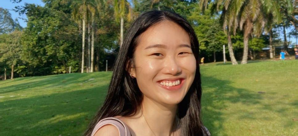 Wen Li, a woman in Malaysia, is smiling in front of a grassy field.