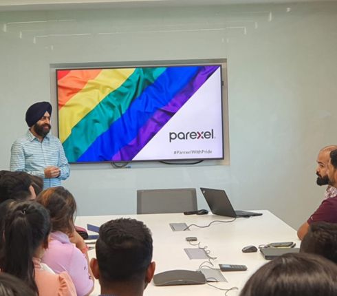 Presenter speaking to a group in a conference room with a Parexel logo displayed on a screen behind him.