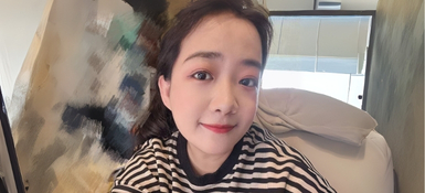 Iris, a Chinese woman, with tied back long dark hair. Wearing a white and dark striped long sleeved top